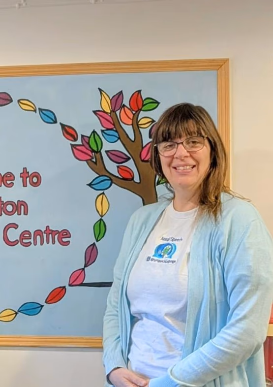 Anna Sellers smiling in front of a colourful communication centre display.