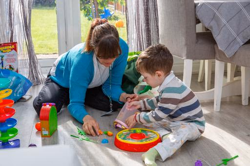 Anna sitting on the floor with a young child during a play-based speech and language therapy activity.